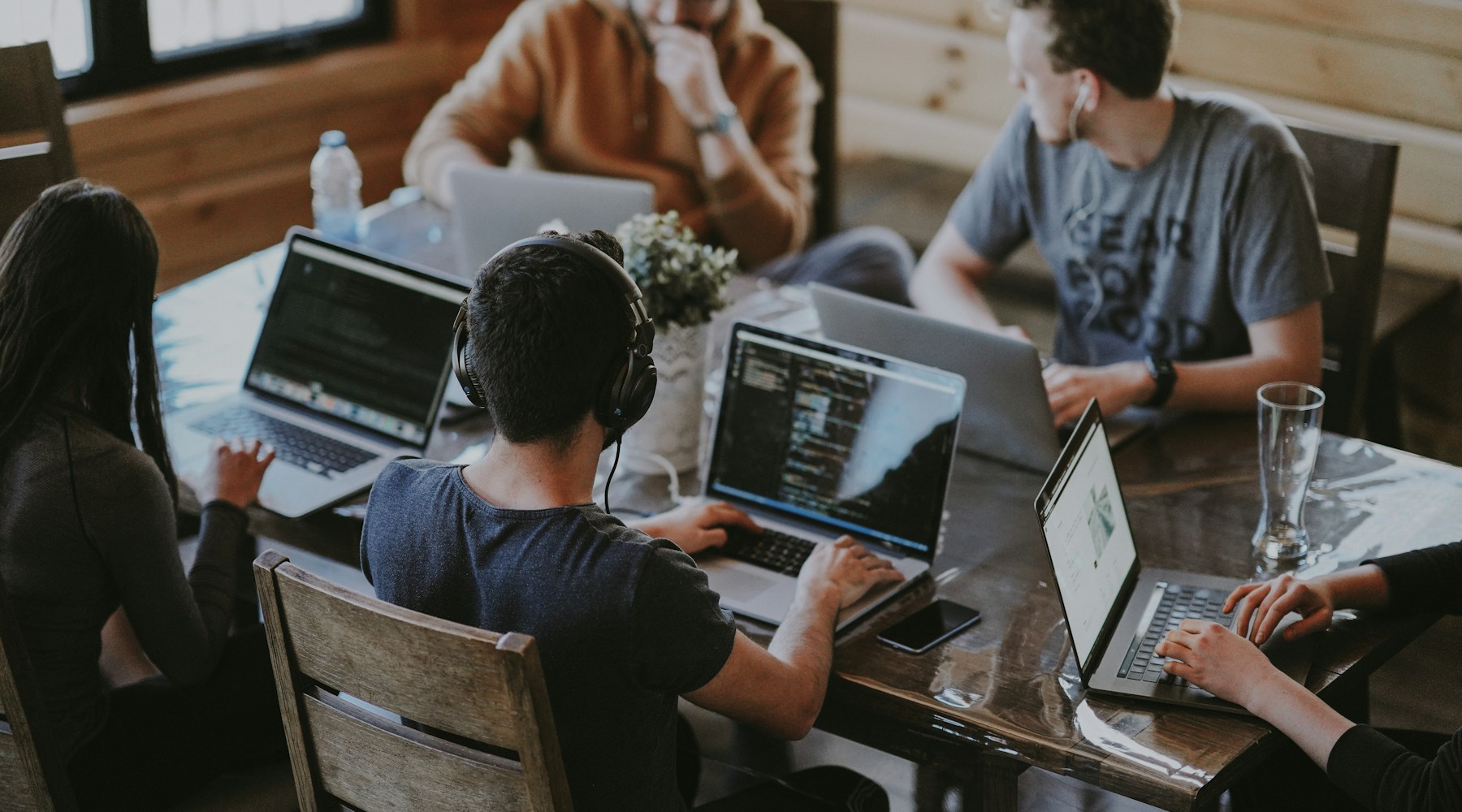 Cinco pessoas em volta de uma mesa de madeira, cada uma com um laptop aberto.