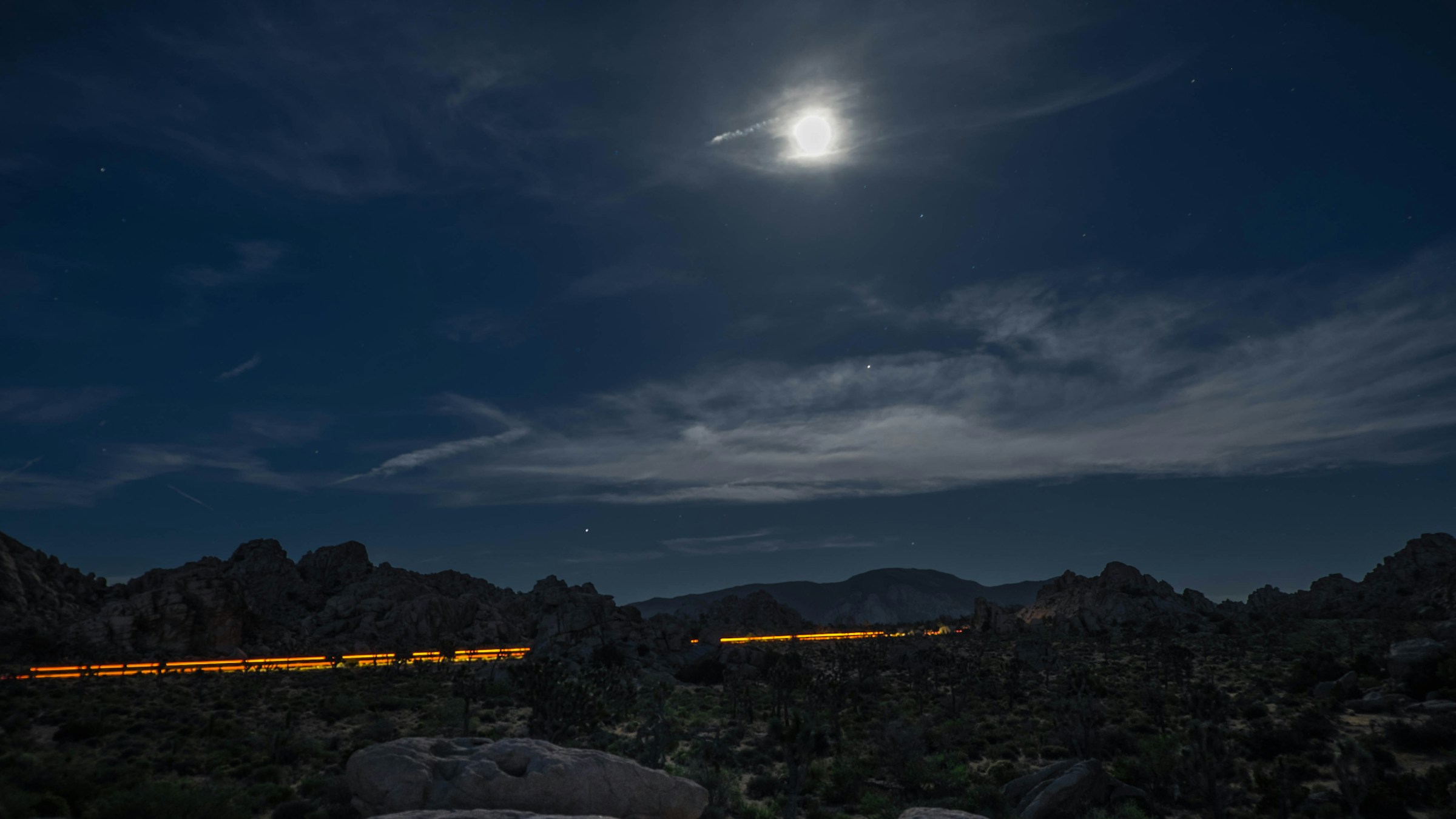 Paisagem noturna sob a luz da lua, com um rastro de luz atravessando as montanhas.